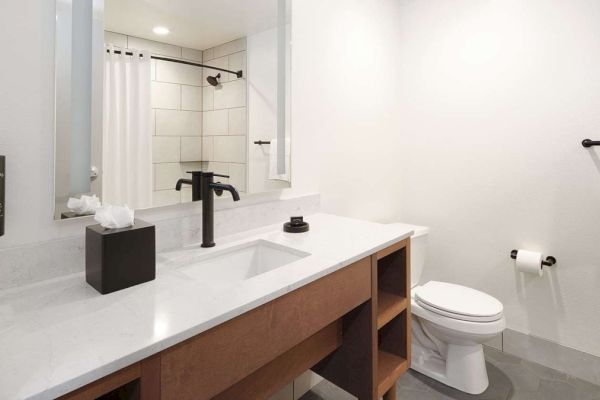 A modern bathroom with a sink, black faucet, mirror, shower, toilet, and towel rack.