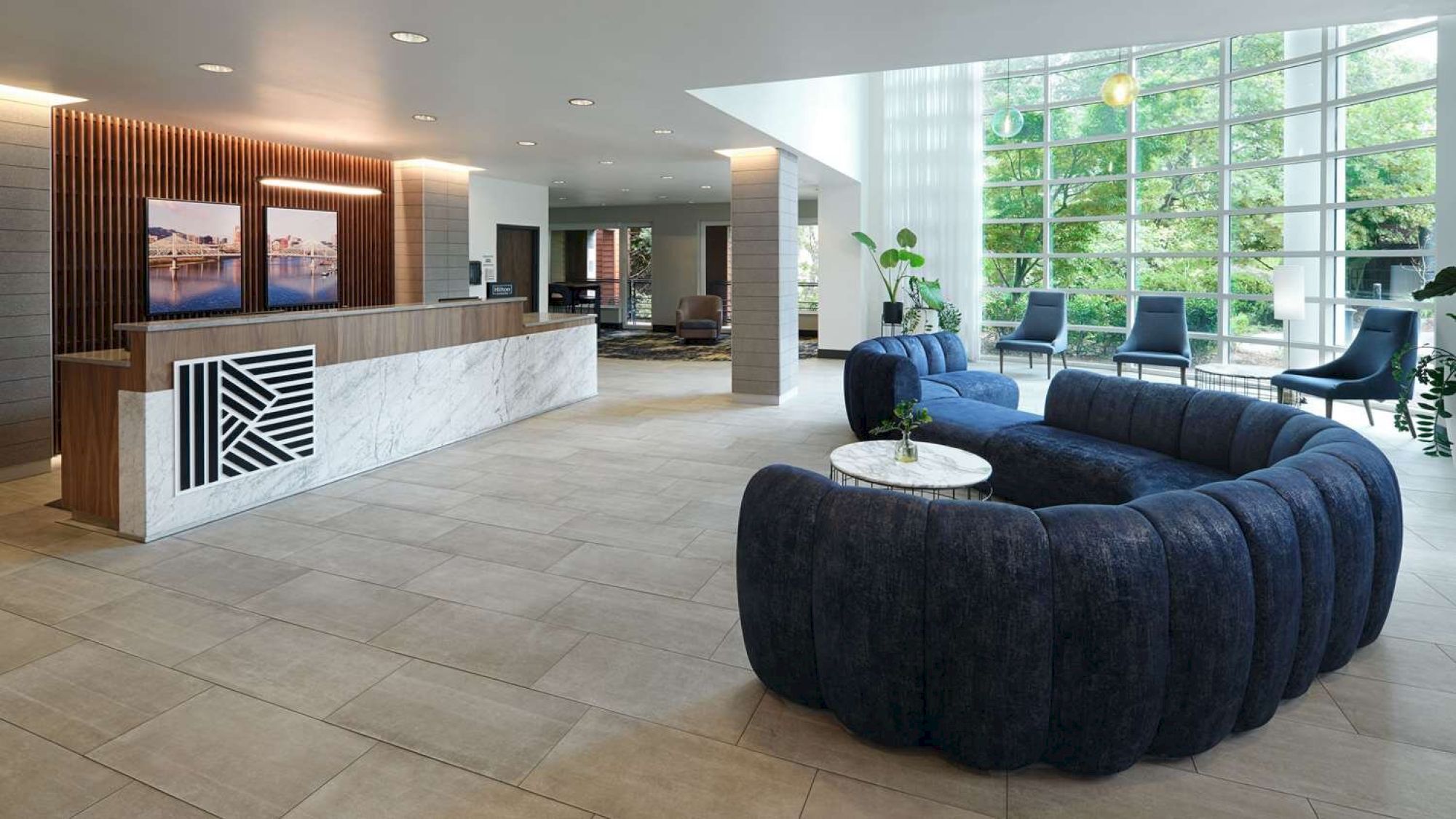 A modern lobby with a marble reception desk, blue velvet seating, large windows, and stylish decor, creating a welcoming atmosphere.