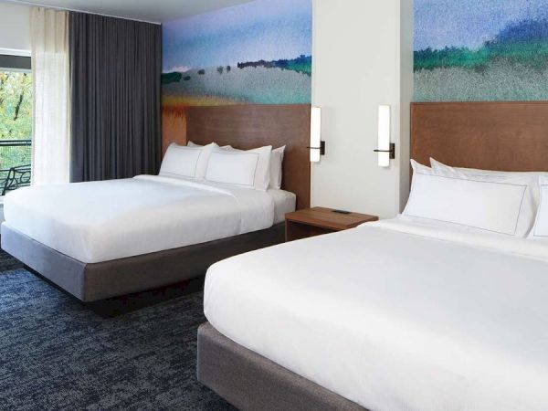 The image shows a hotel room with two large beds, a colorful wall mural, a window with a view, and modern lighting fixtures.