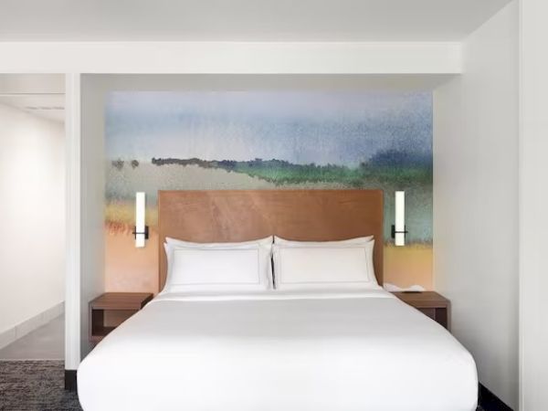 A minimalist hotel room with a large bed, artistic headboard, and subtle lighting, creating a cozy atmosphere.