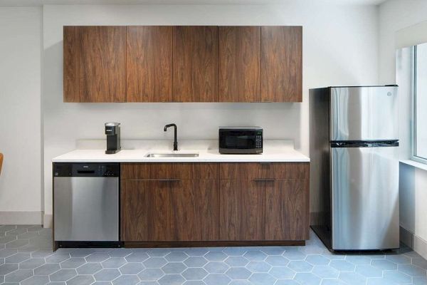 The image shows a kitchen with wooden cabinets, a fridge, a dishwasher, a sink, a coffee maker, and a microwave.