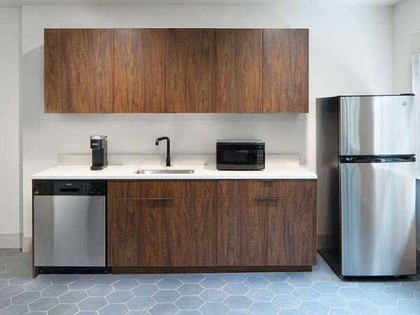 The image shows a kitchen with wooden cabinets, a fridge, a dishwasher, a sink, a coffee maker, and a microwave.