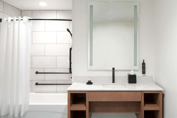 A modern bathroom with a white-tiled shower, a curtain, a sink with a mirror, and black fixtures.