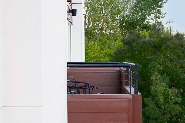 A row of balconies with outdoor furniture on a white building, surrounded by green trees and a clear blue sky.