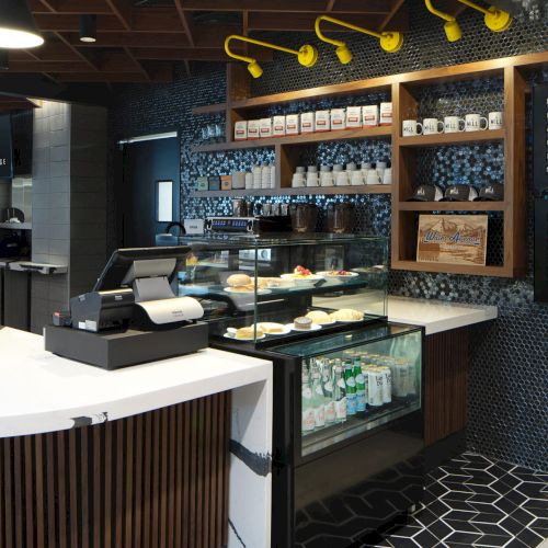 This image shows a modern coffee shop with a counter, pastries on display, a menu board, and a stylish interior design.