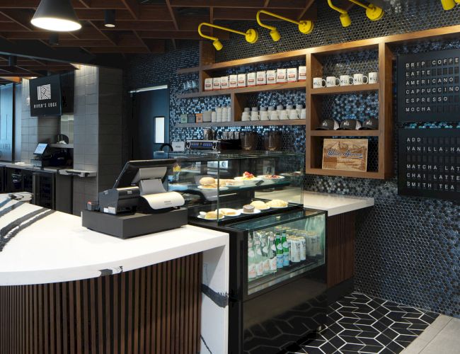 This image shows a modern coffee shop with a counter, pastries on display, a menu board, and a stylish interior design.