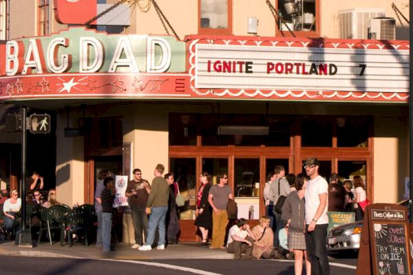 People are gathered outside the Bagdad Theater, which has a marquee that reads "Ignite Portland 7," indicating an event.