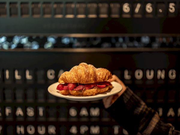 A croissant sandwich on a small plate being held up in front of a vintage signboard display.